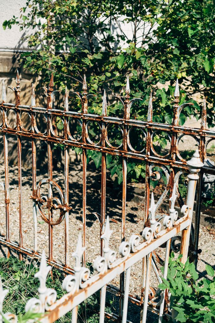 hero-img-01 Close-up of a decorative rusty metal garden fence on a sunny day.