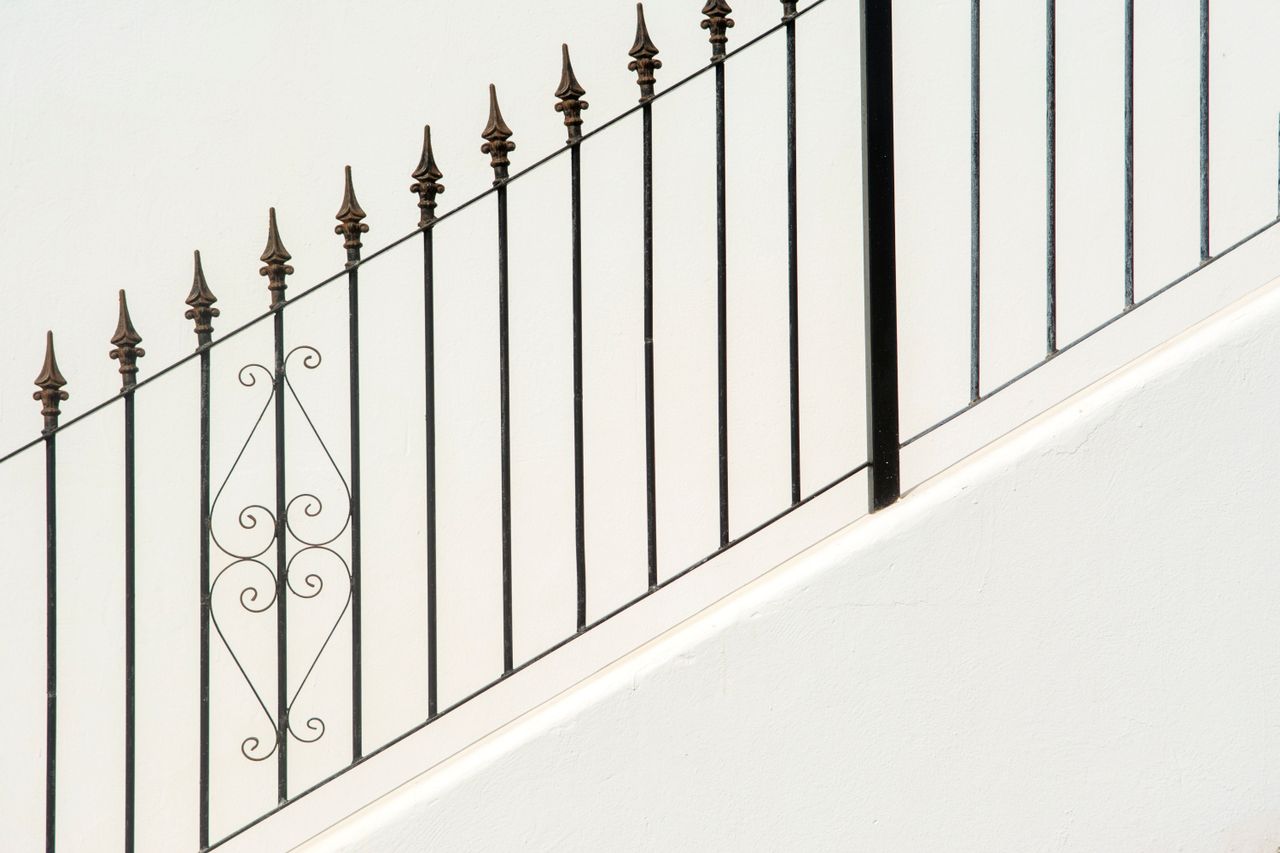 why-choose-us Diagonal metal railings with decorative elements against a clean concrete wall.